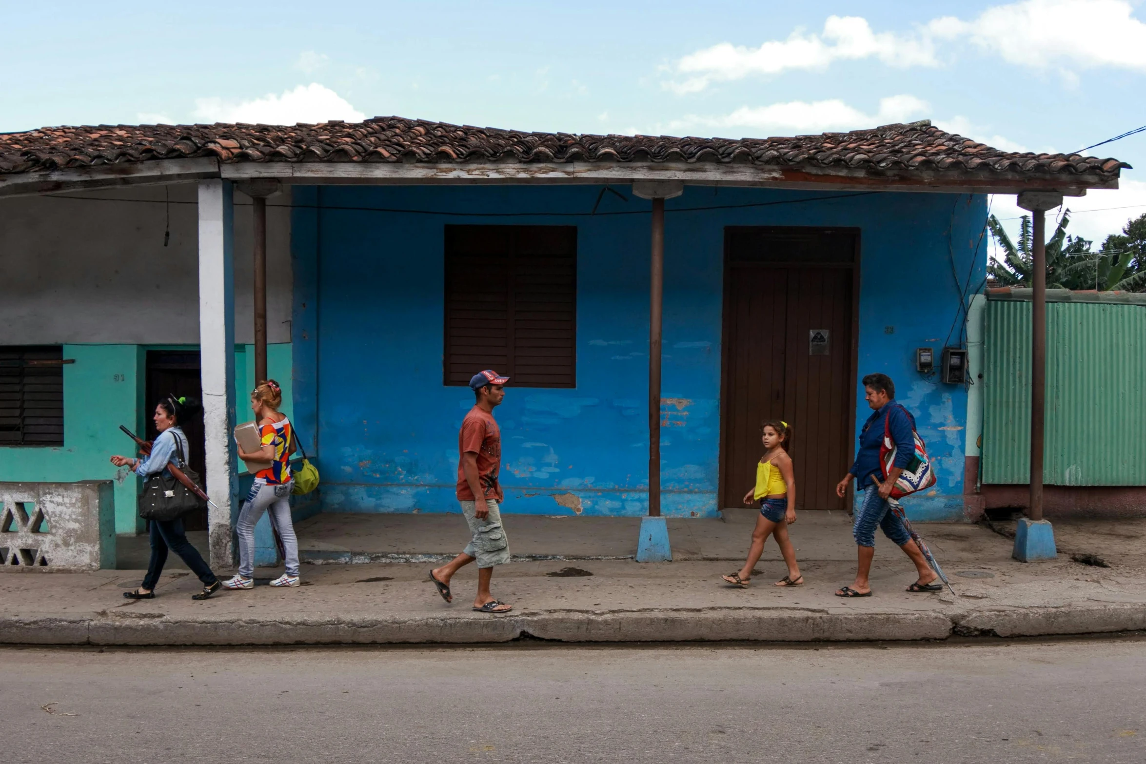 group of people crossing the street, walking by a colorful house