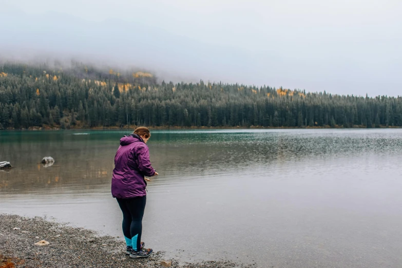 a woman standing in the water next to a forest