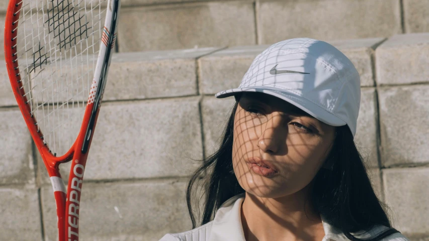 a woman is holding a tennis racket by a brick wall