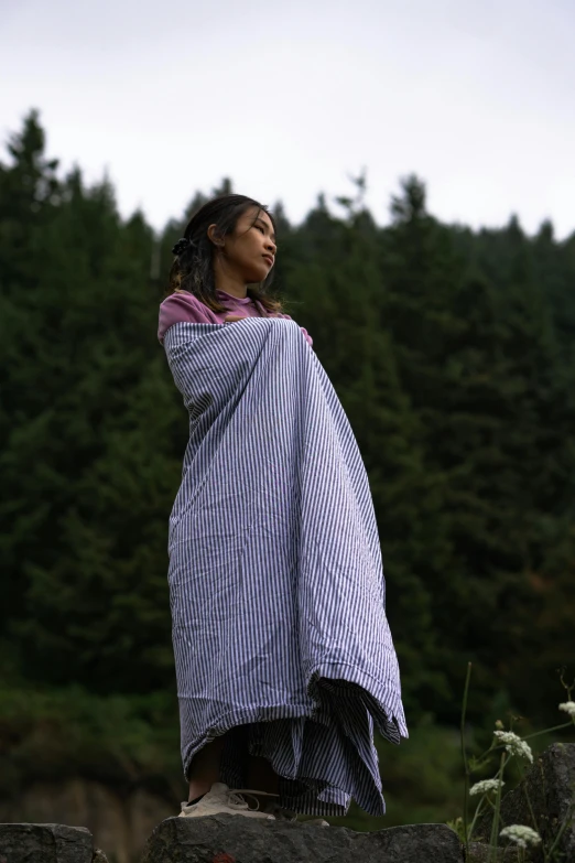 a woman wrapped in a striped blanket by trees