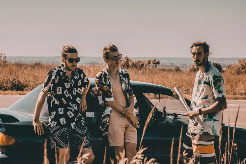 three men wearing shirts and shorts next to a car