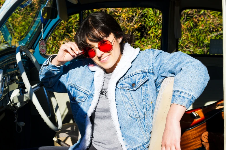 a woman with sunglasses and jacket in front of a car talking on the phone