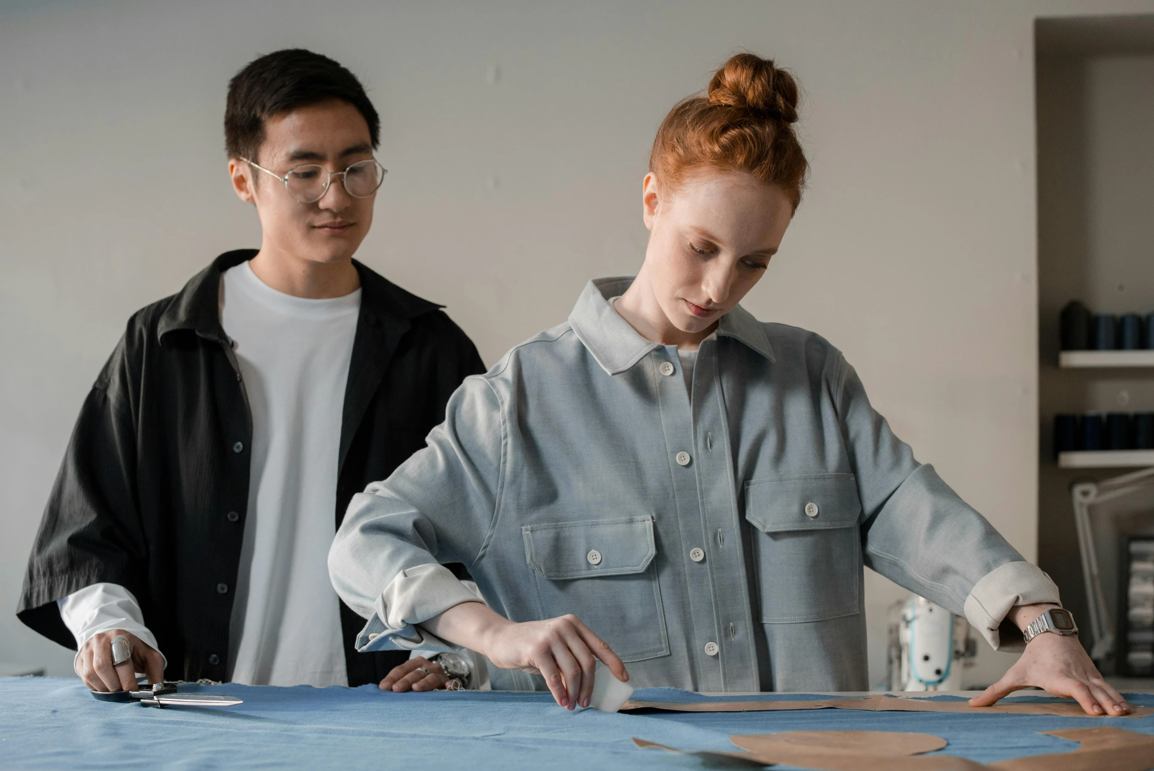 two people working on a table and sewing together