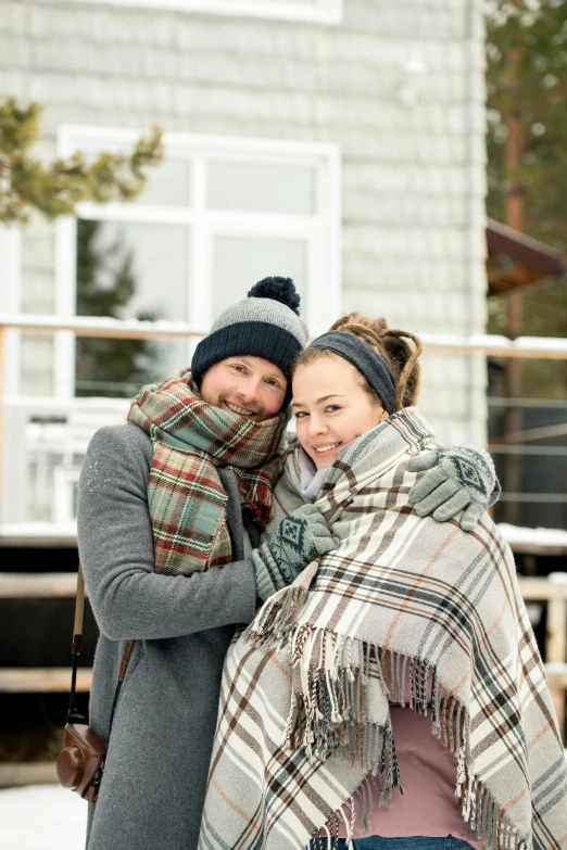 two women wrapped up with a plaid blanket standing in front of a house