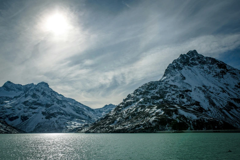 the mountains next to the lake are covered in snow