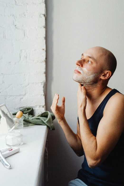 a man is shaving his beard by a window