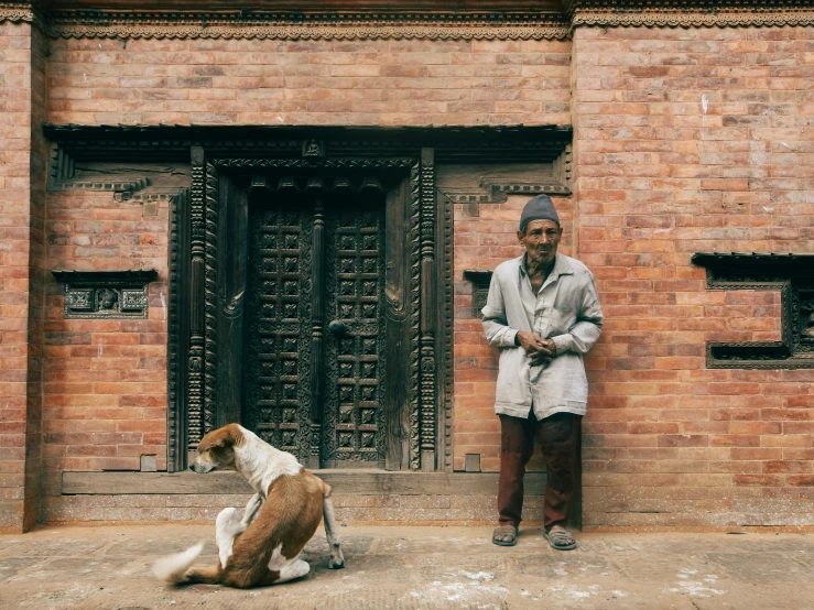 a man standing in front of a brick wall next to a brown dog