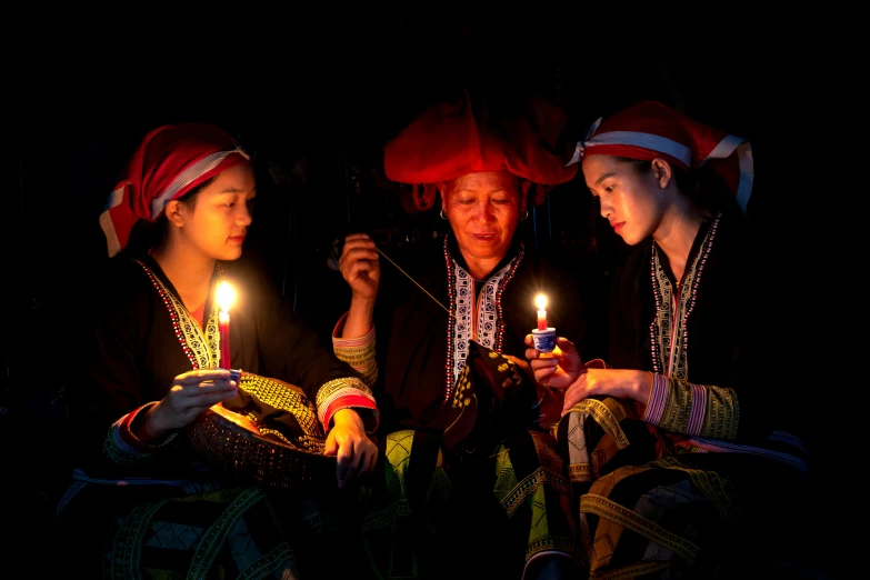 three people sitting around a table holding candles in their hands