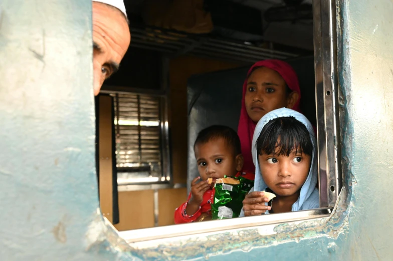 three children eating snack from their mother on a train