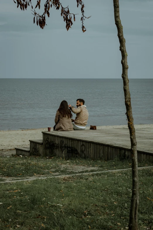 three people sitting at a pier with an ocean in the background