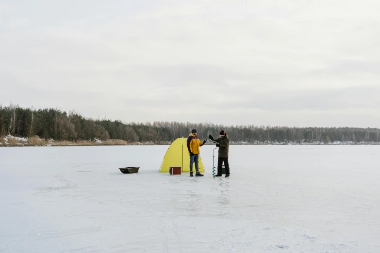 two men standing on a frozen lake standing next to a yellow tent