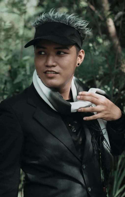 a young man wearing a black hat while standing near a lush green forest