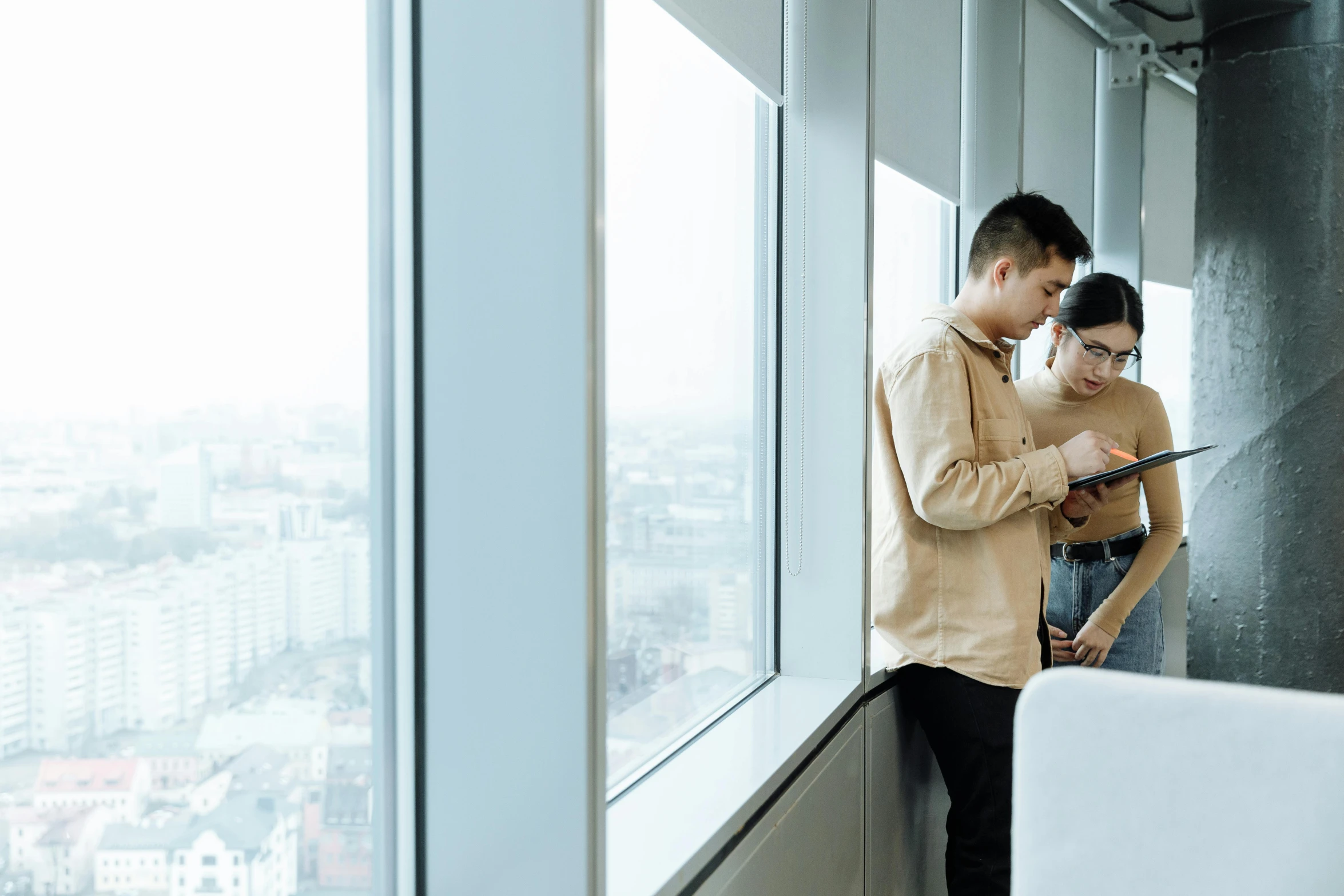 a man and woman look out a window with an tablet