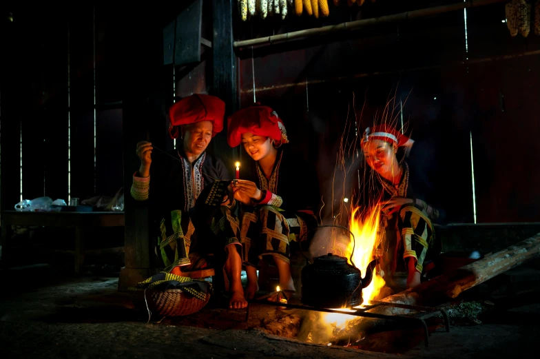 three people are sitting in front of a bonfire