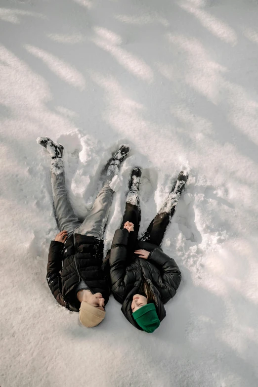 two people laying down in the snow while they are holding hands and posing for the camera