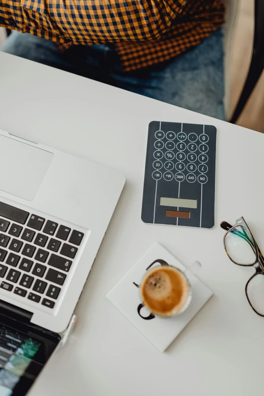 a laptop computer with a passport, glasses and cup of coffee on top