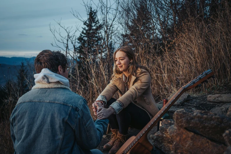 a man and woman holding hands sitting on a rock in the woods