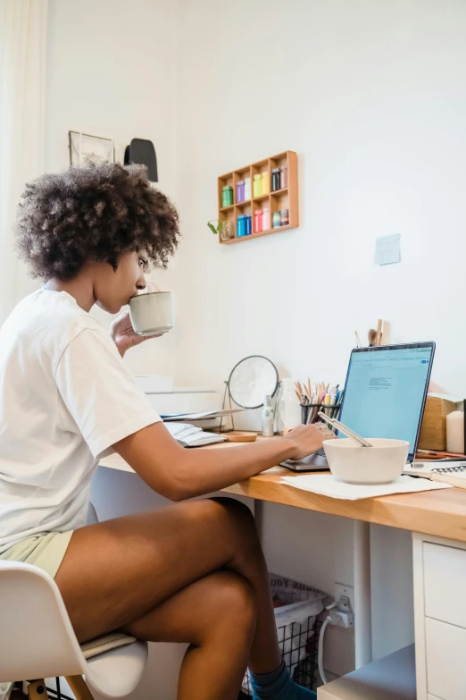 the woman is sitting at a computer desk using her laptop