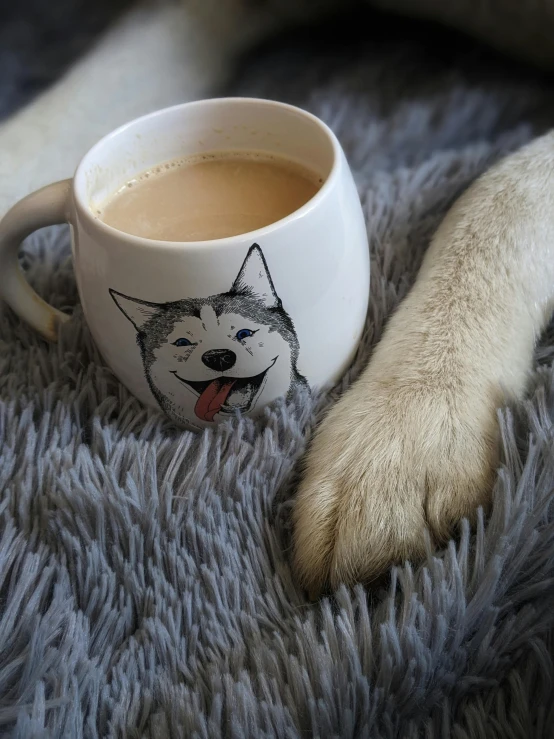 a white cup with a dog's face and tail on it, next to a black cat paw