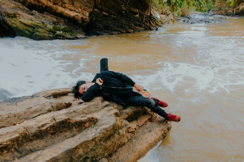 there is a person lying on a rock by a river