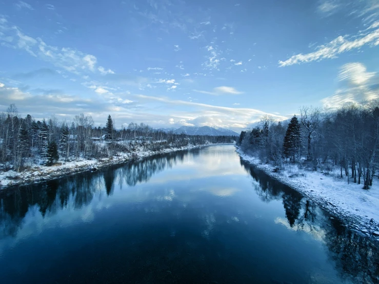 the blue water is lined with trees and snow