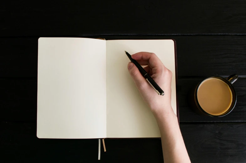 someone is writing in a notebook next to a cup of coffee