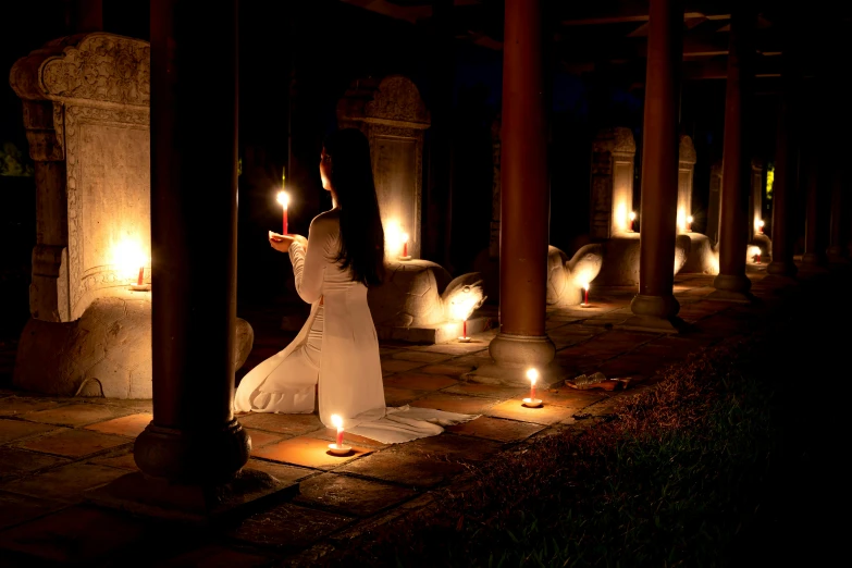 a woman in white dress holding candles in front of her head