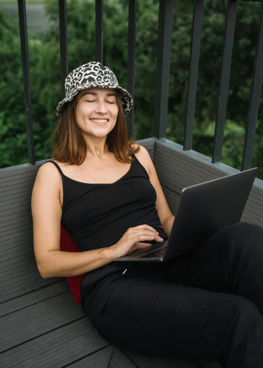 a smiling woman is using her laptop on the bench