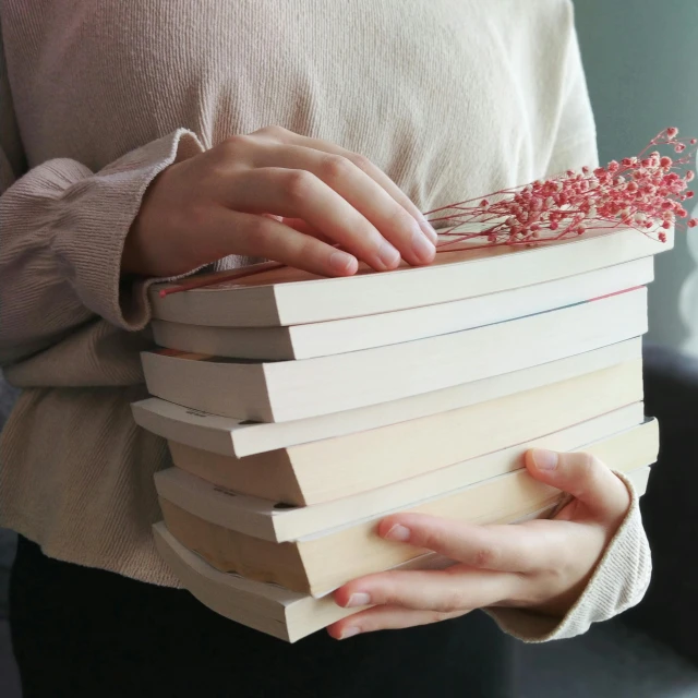 a woman holding several books that have some dried flowers on top of them