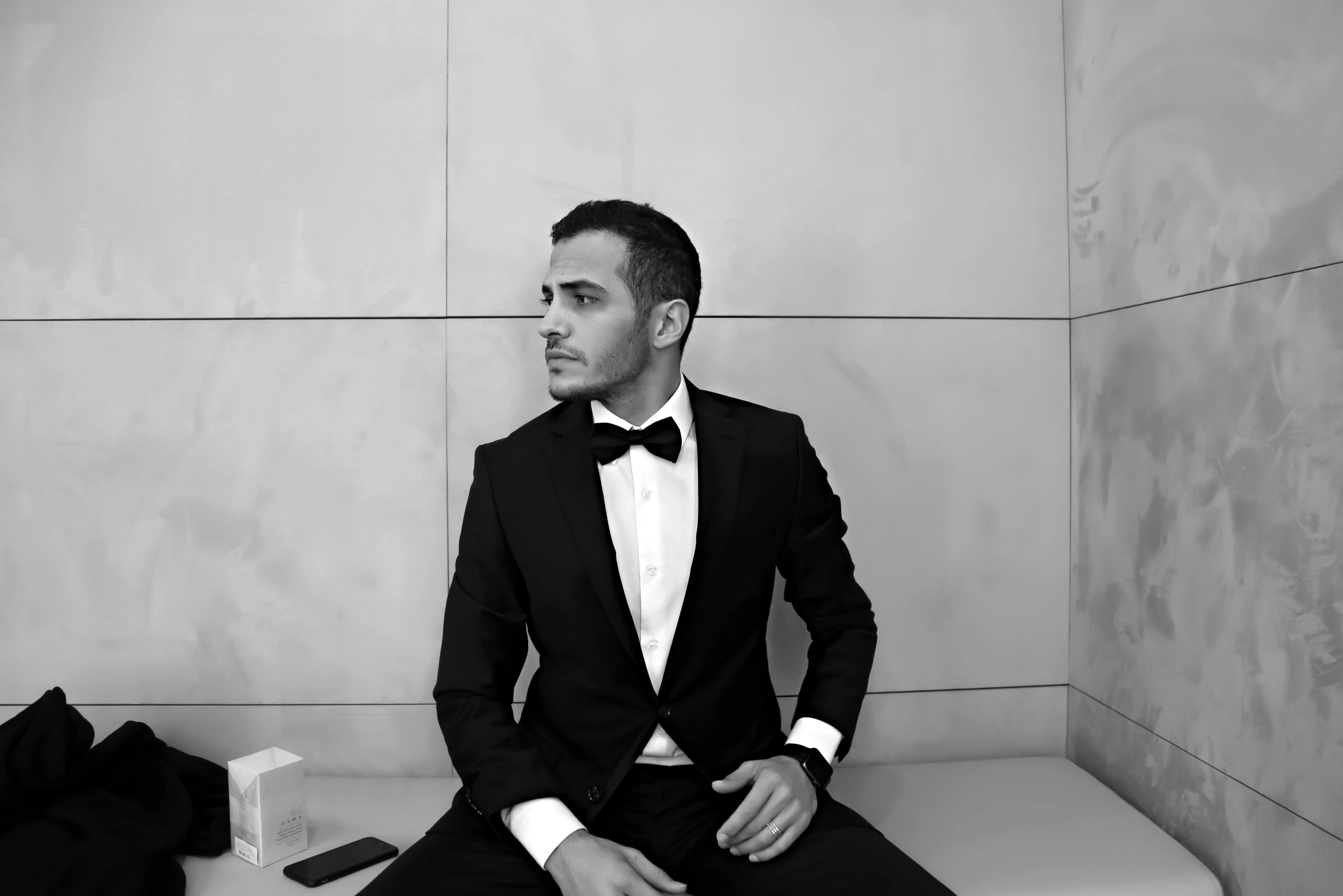 black and white po of man in tuxedo sitting on a bench