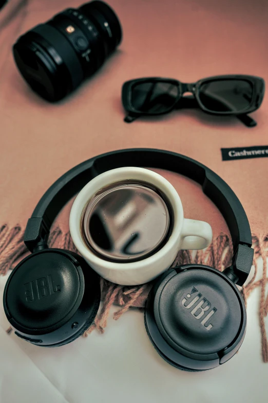 a cup of coffee, headphones, and some sunglasses sit on a bed