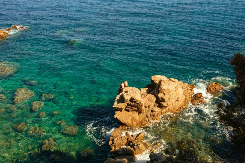 two large rocks near the water with one man jumping off