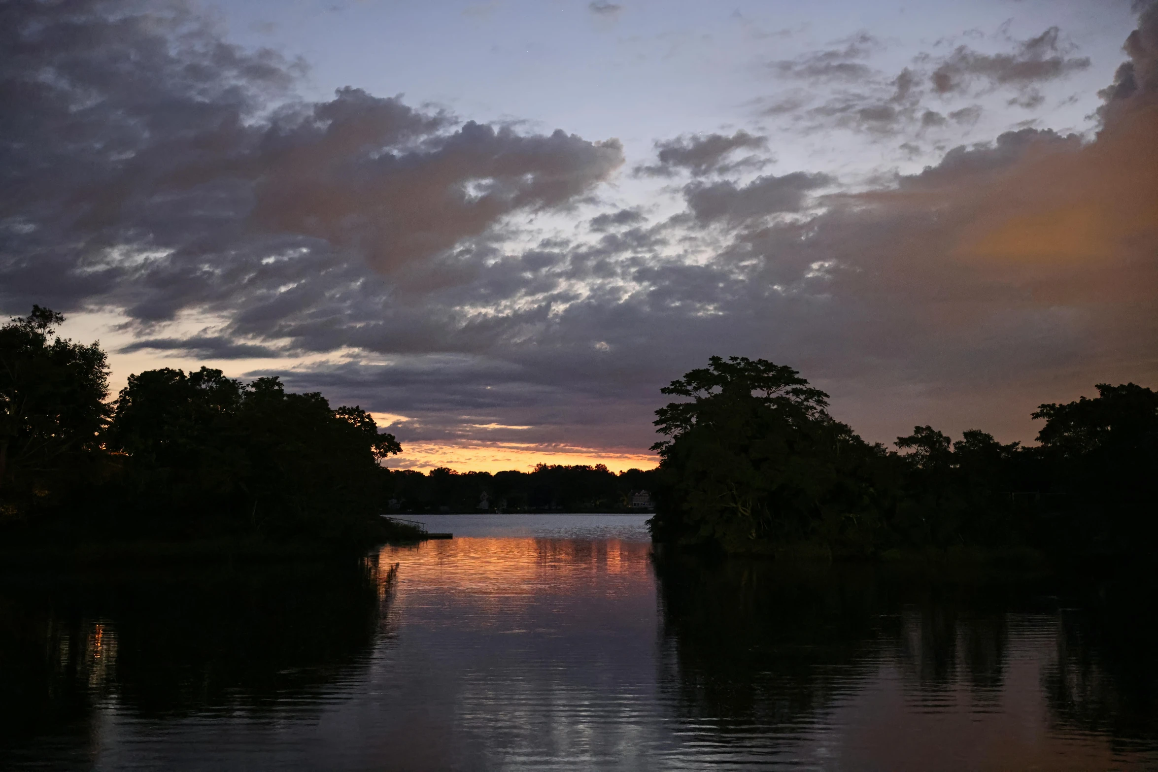 the clouds are setting over the lake where the trees are in bloom