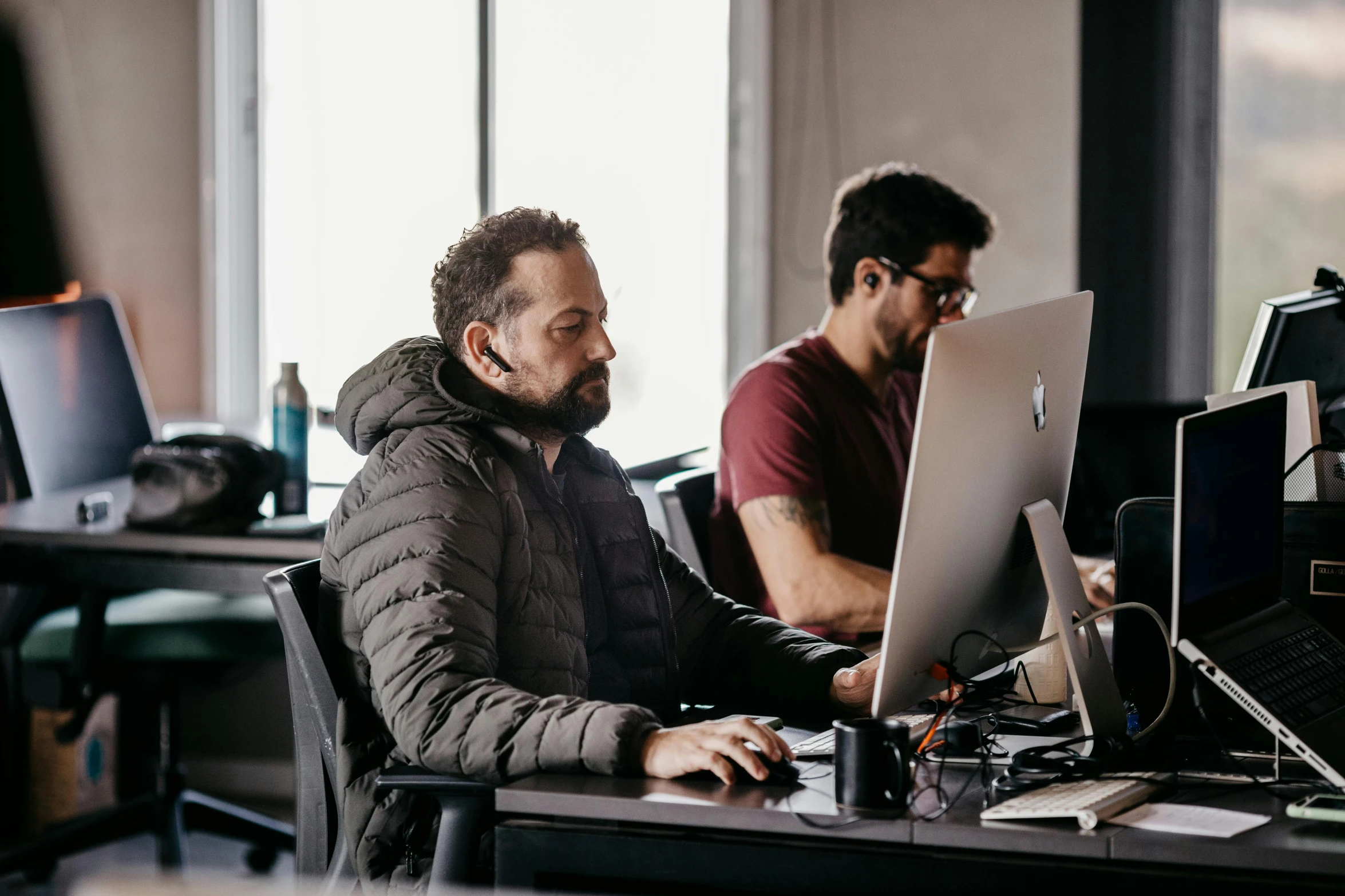 two men sitting in front of computers on top of desks