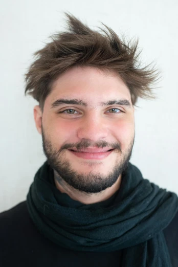 a man with a beard smiles while wearing a scarf