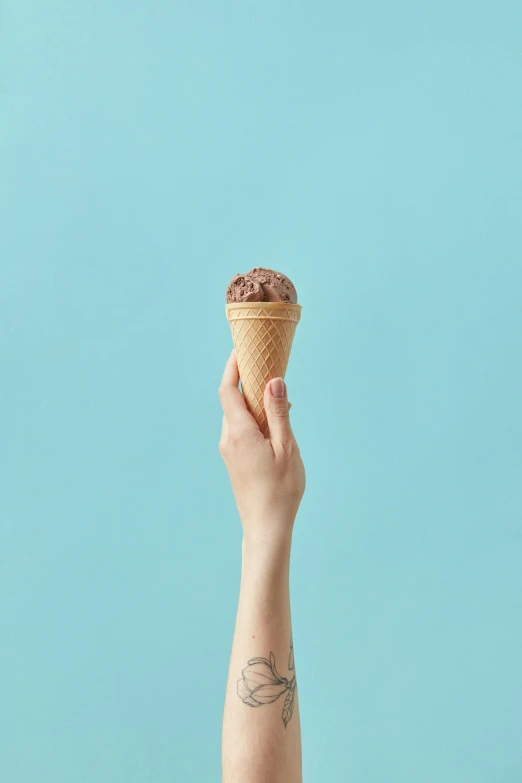 hand holding an ice cream cone over turquoise background