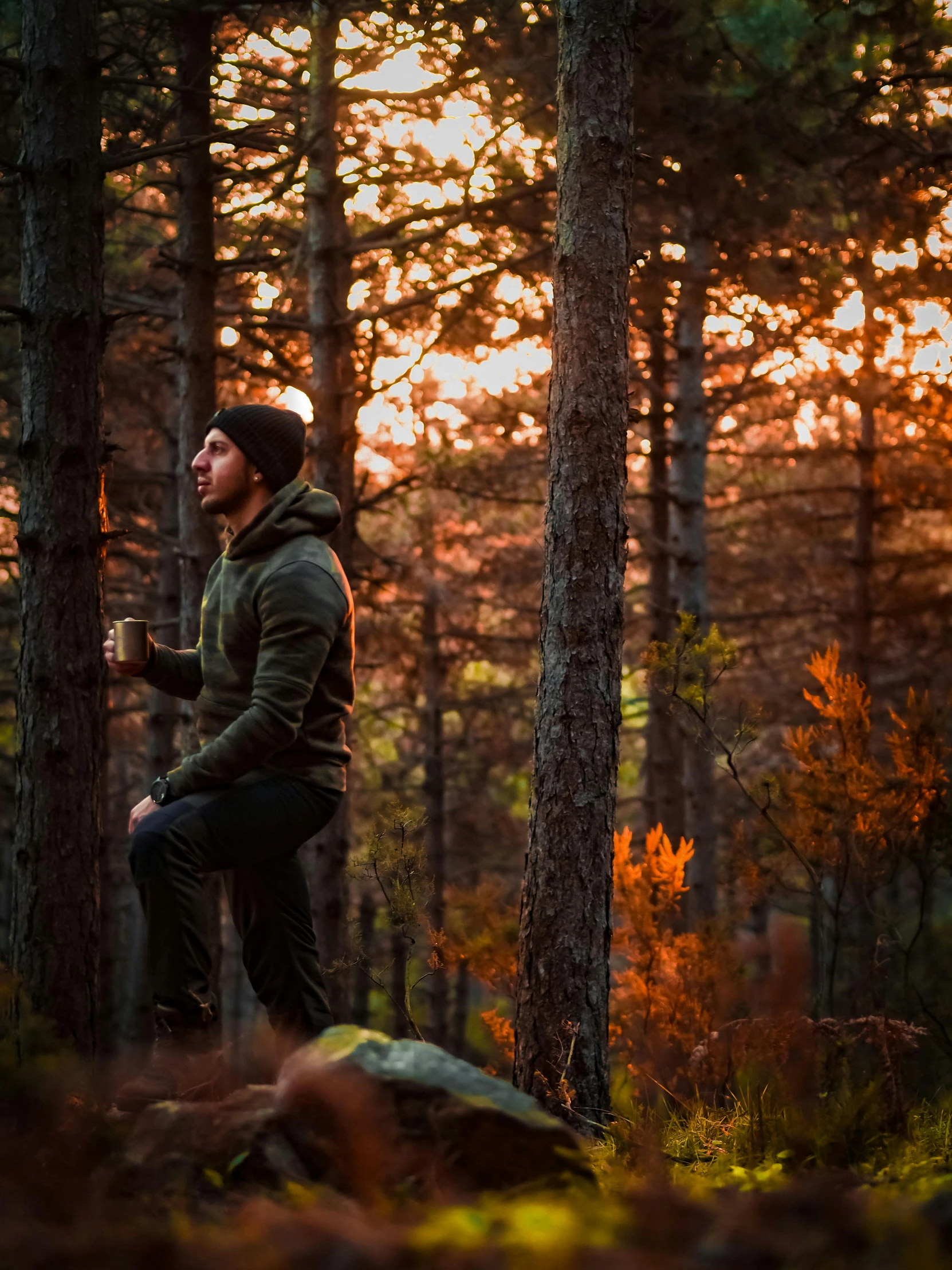 man sitting on rock in middle of forest drinking a beverage