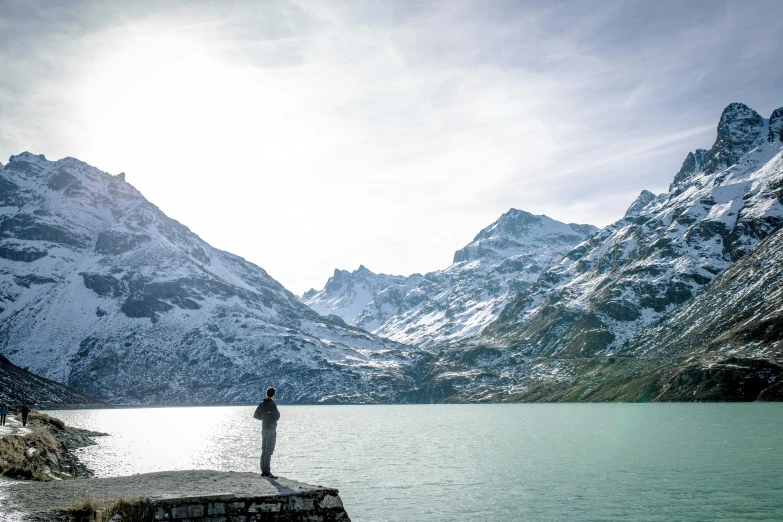 a man stands on a ledge and fishes at the edge of a mountain lake