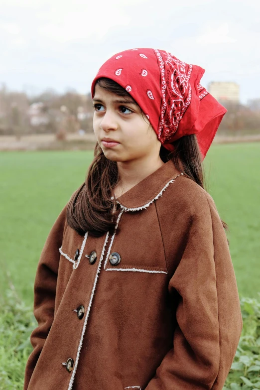 a little girl is standing in the field wearing a red bandanna