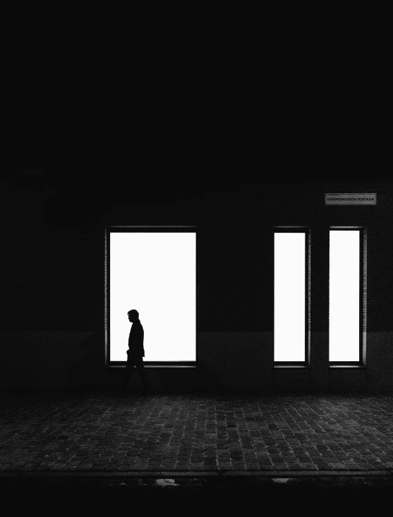 a person walking in the dark near three open windows