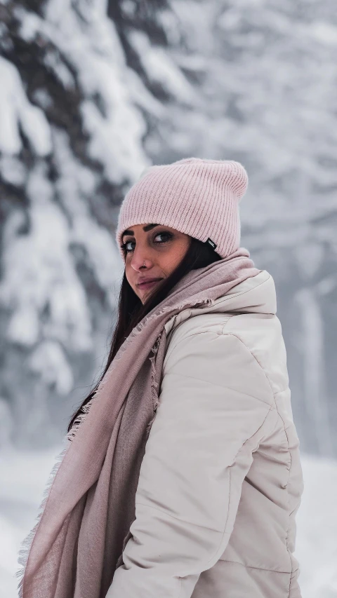 a woman with a hat on holding her scarf in the snow