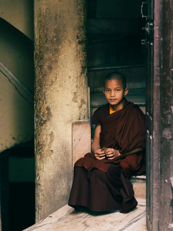 a young monk is seated on the steps of an old building