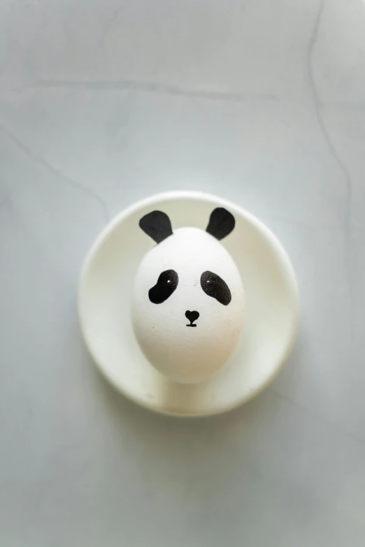 a white bowl has an egg shaped like a panda face on it