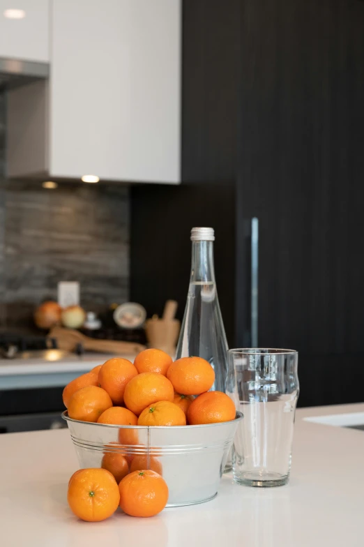 the oranges are in a silver bowl and glass on a white table