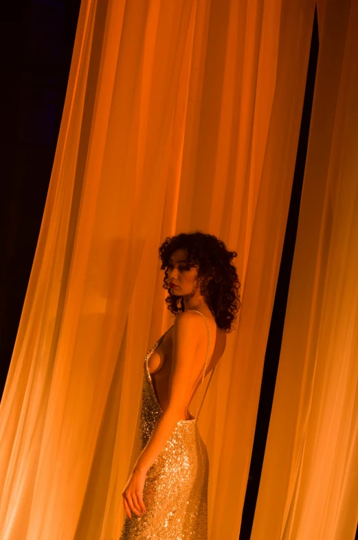 a woman standing in front of an orange curtain