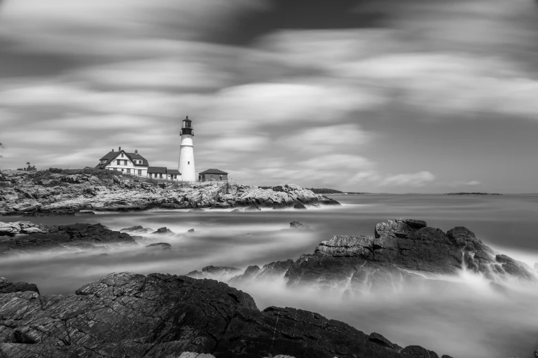 black and white pograph of lighthouse on rocky shoreline