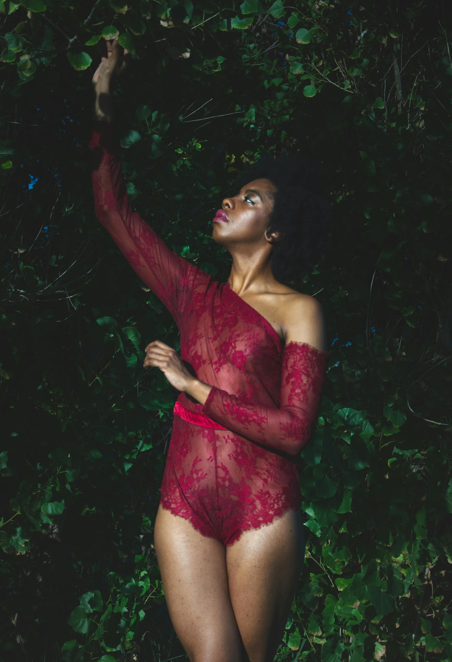 a woman in a red bodysuit is standing near some bushes