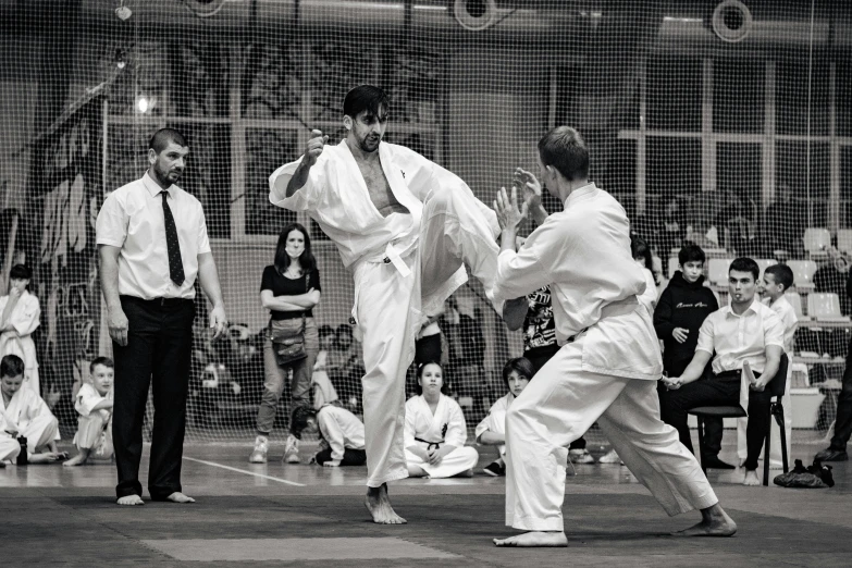 two men with white uniforms practicing martial in front of a crowd