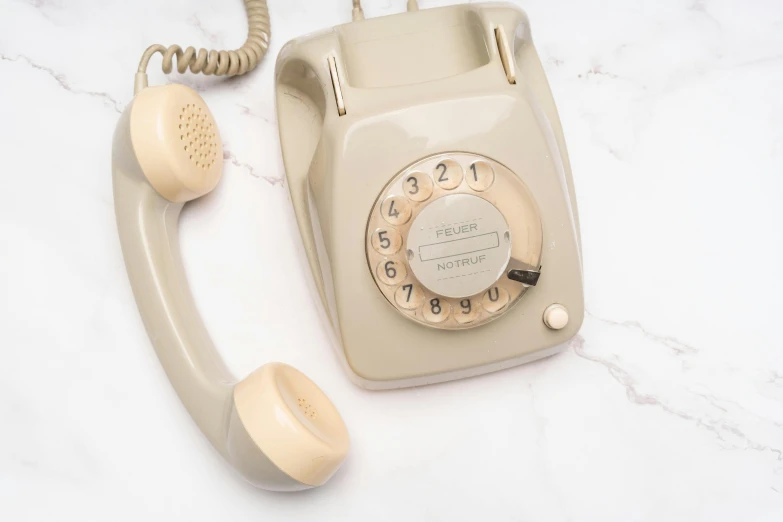 a cream - colored rotary telephone and dial, on a marble table