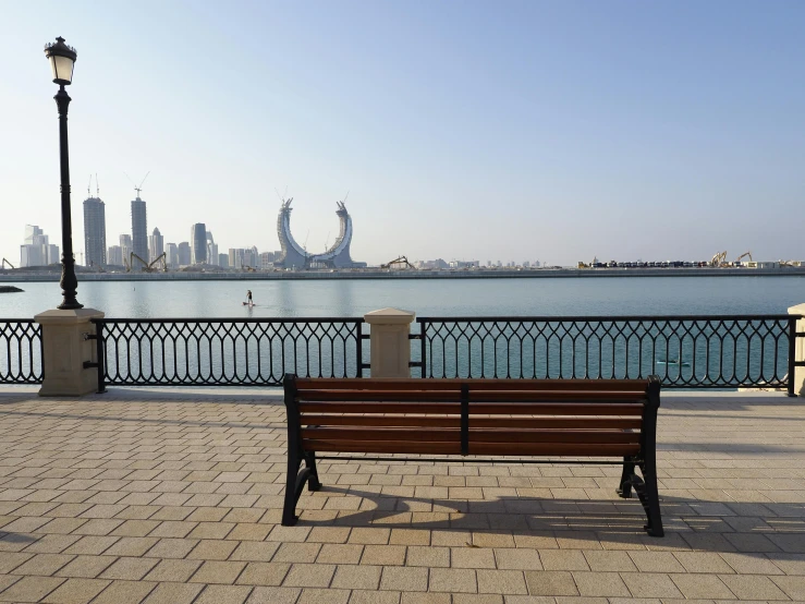 an empty bench is in front of the water with a cityscape